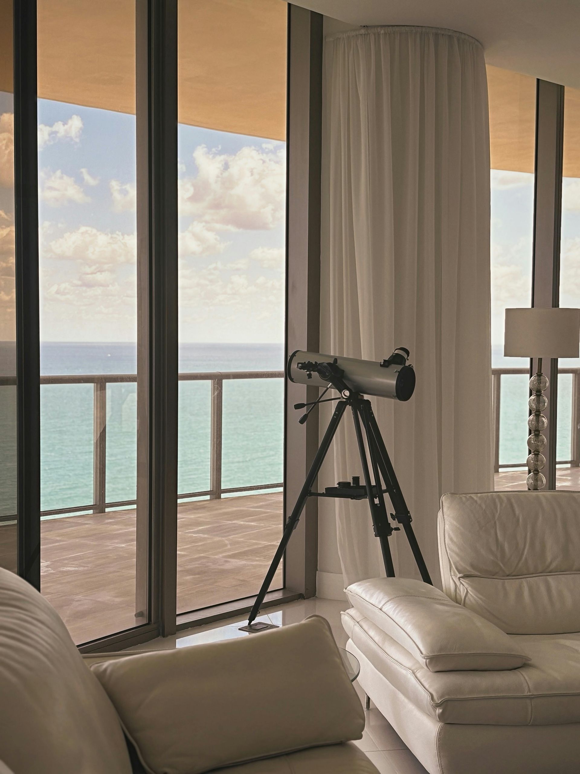 Living room with telescope facing the ocean through floor-to-ceiling windows