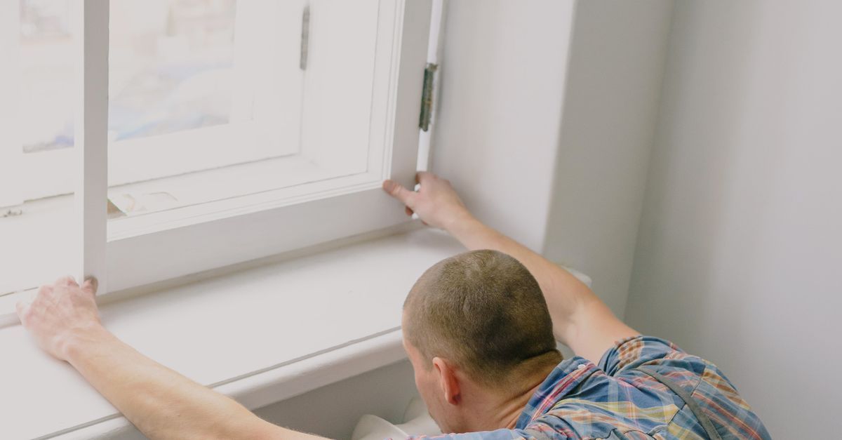 Person reaching toward a bright window sill from inside a room.