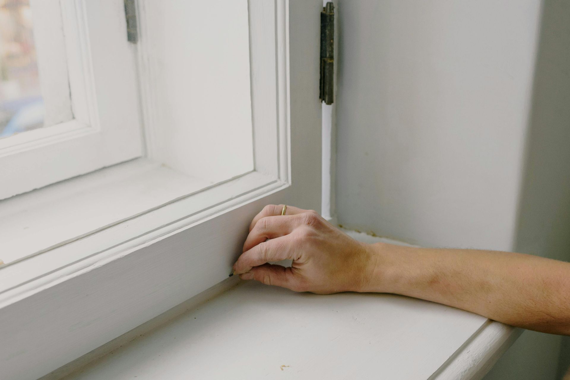 Hand reaching onto a white windowsill beside a white window frame.