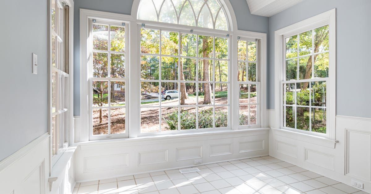 Bright sunroom with large arched windows, white walls, and light tile flooring overlooking a garden.