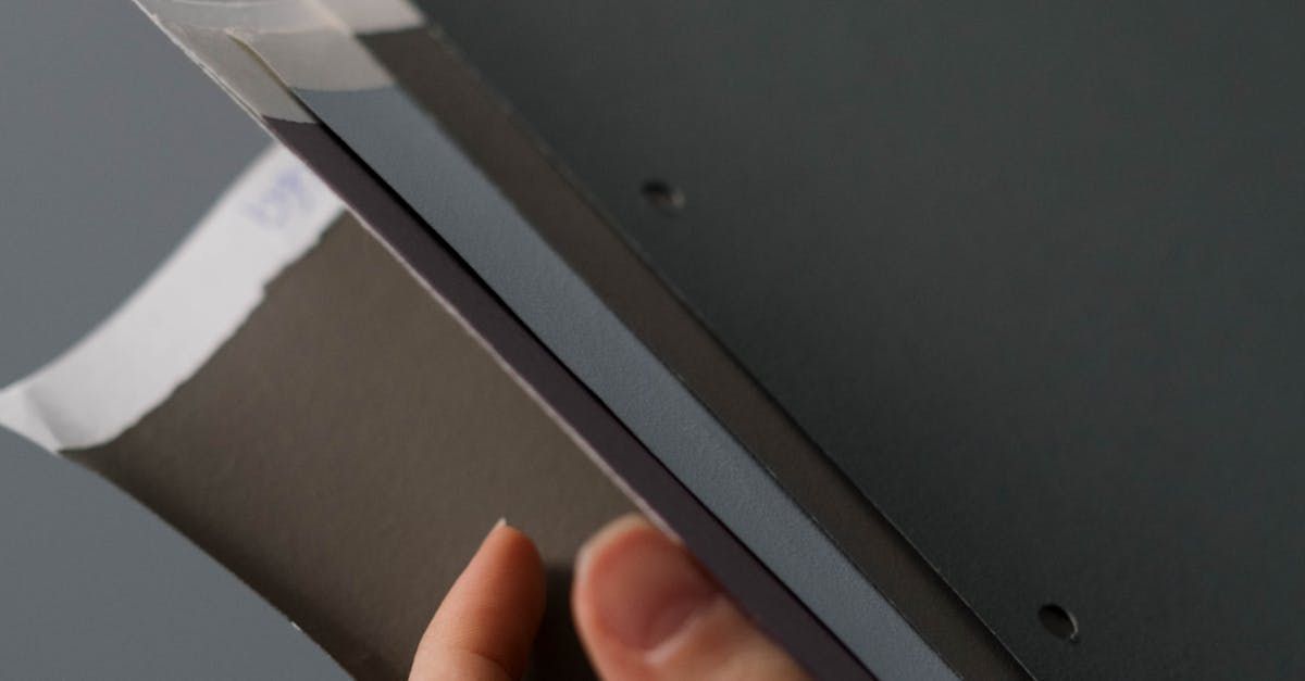 Hand holding a gray and black rectangular object near a dark surface