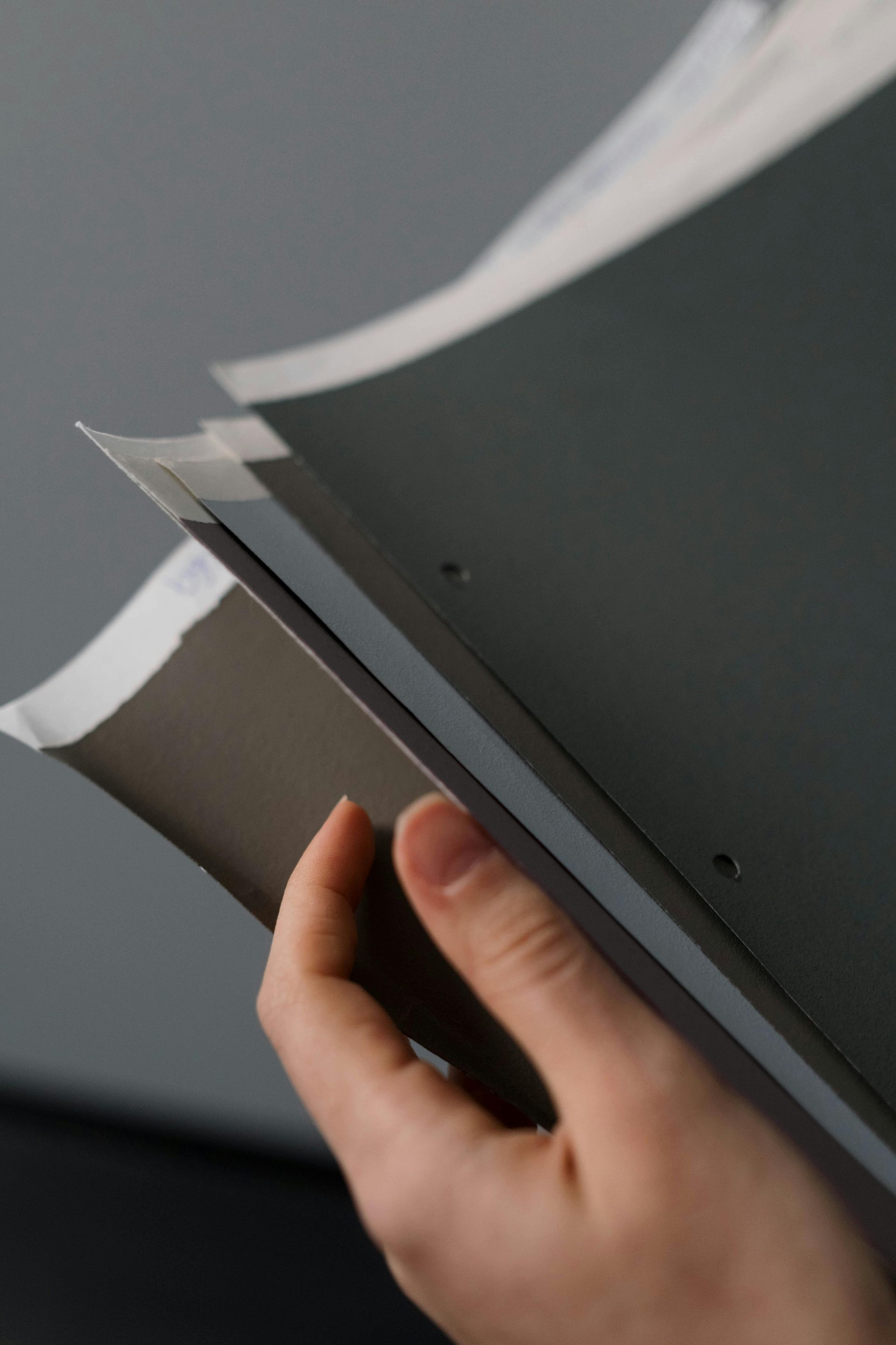 Hand flipping through a gray catalog or booklet against a dark background
