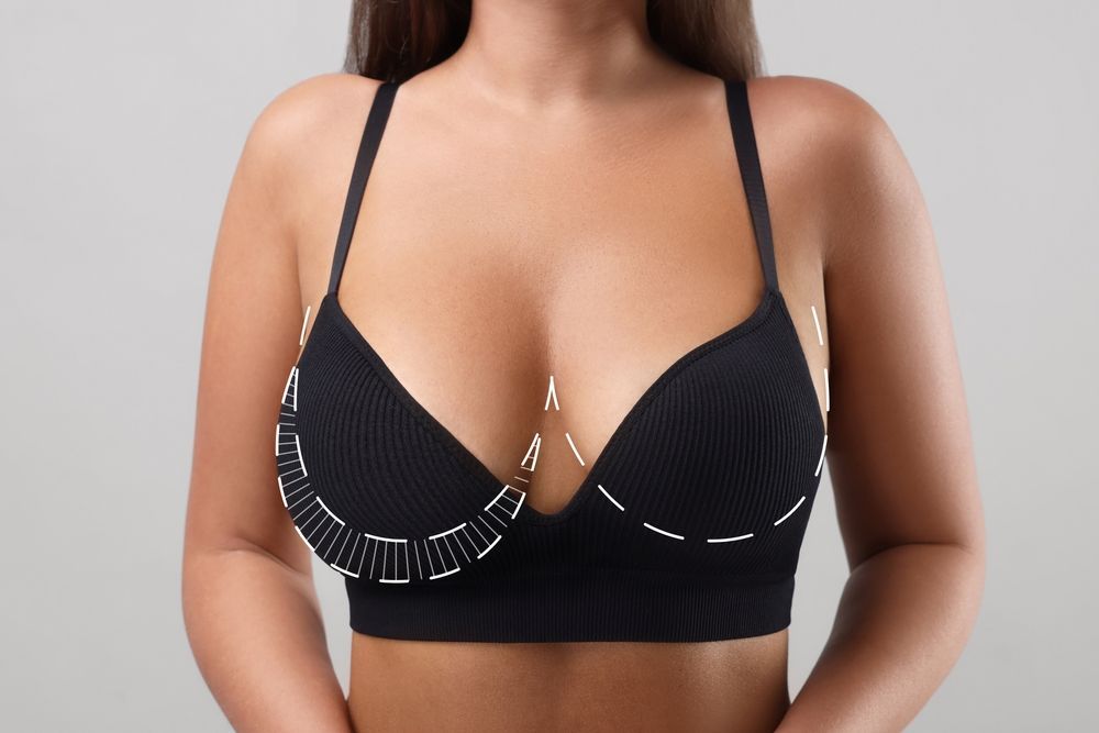 Woman wearing a black bra with white trim and patterned straps, shown from the chest up on a plain background