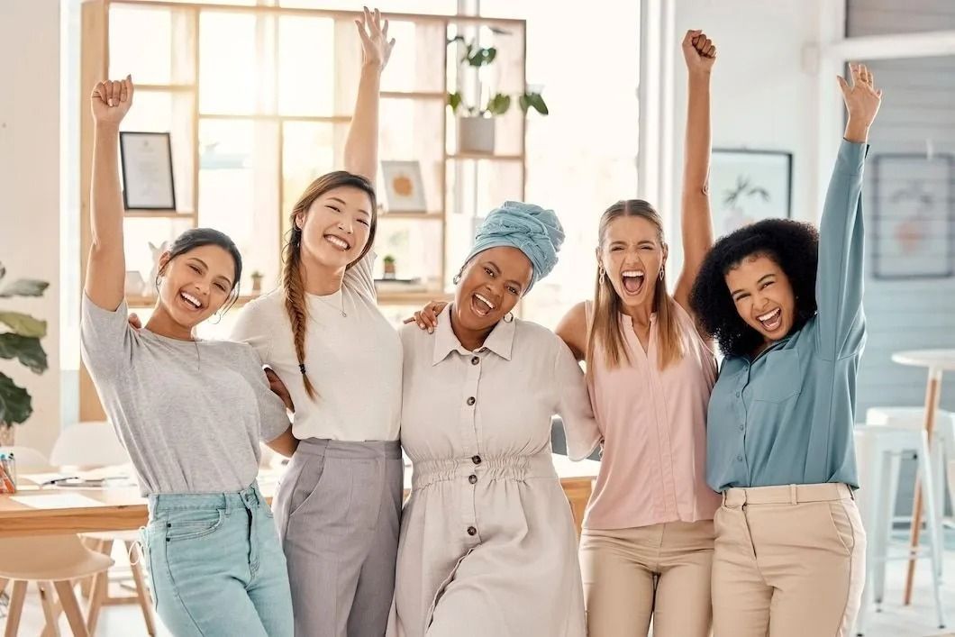 Five people stand side-by-side in a bright, modern office, smiling and cheering with one arm raised in celebration.