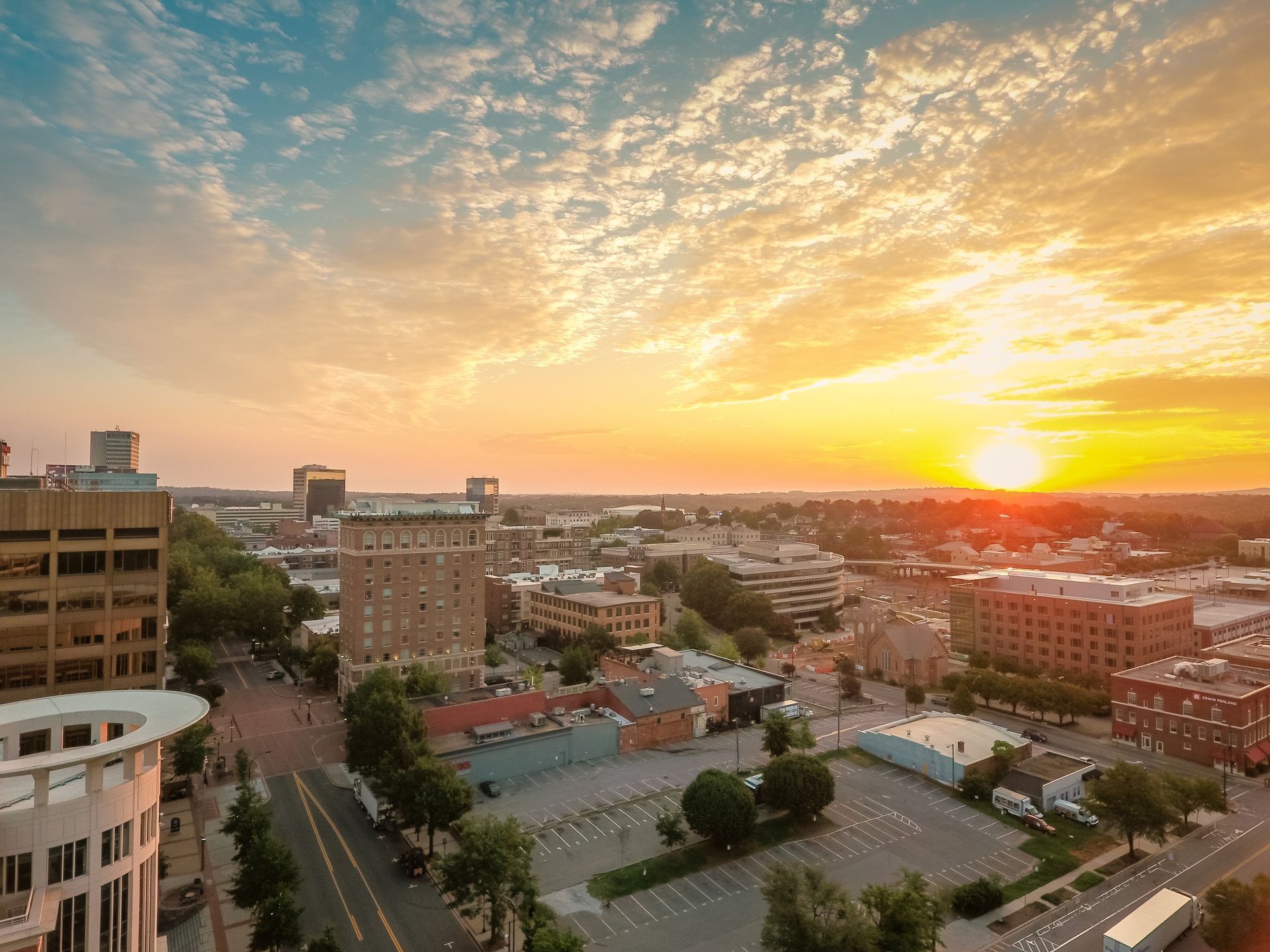 An aerial view of a city at sunset with a parking lot in the foreground.