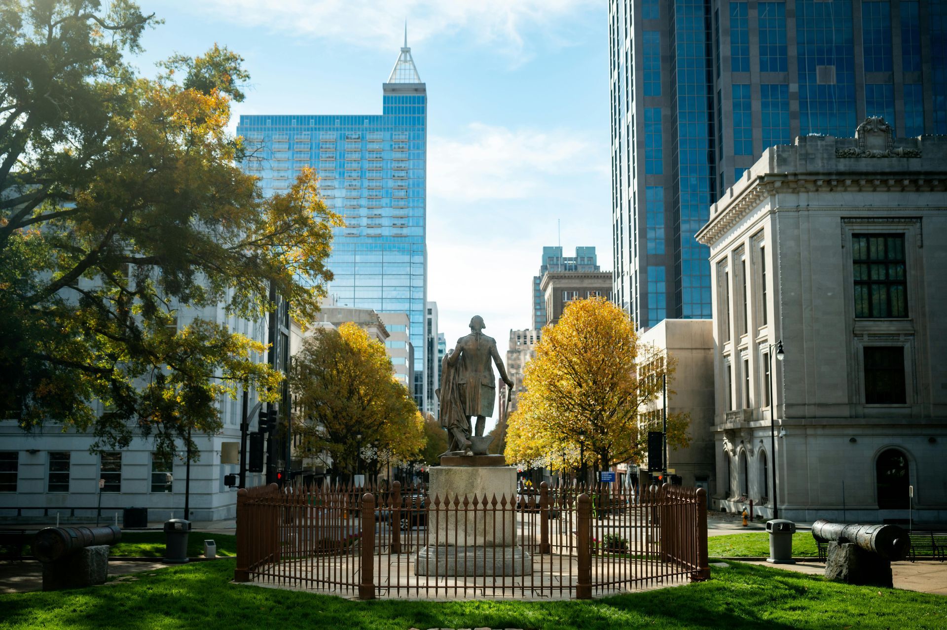 A statue of a man is in the middle of a city park surrounded by tall buildings.