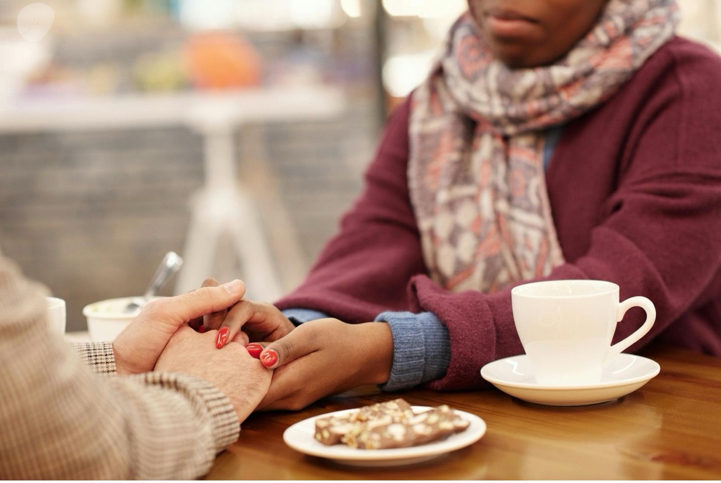 Two people holding hands across a table with coffee cup and cookie.
