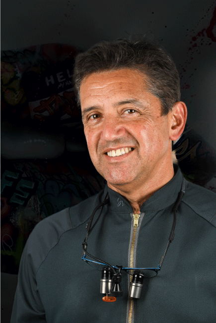 Hombre sonriendo, con camiseta verde azulado y gafas. Fondo negro.