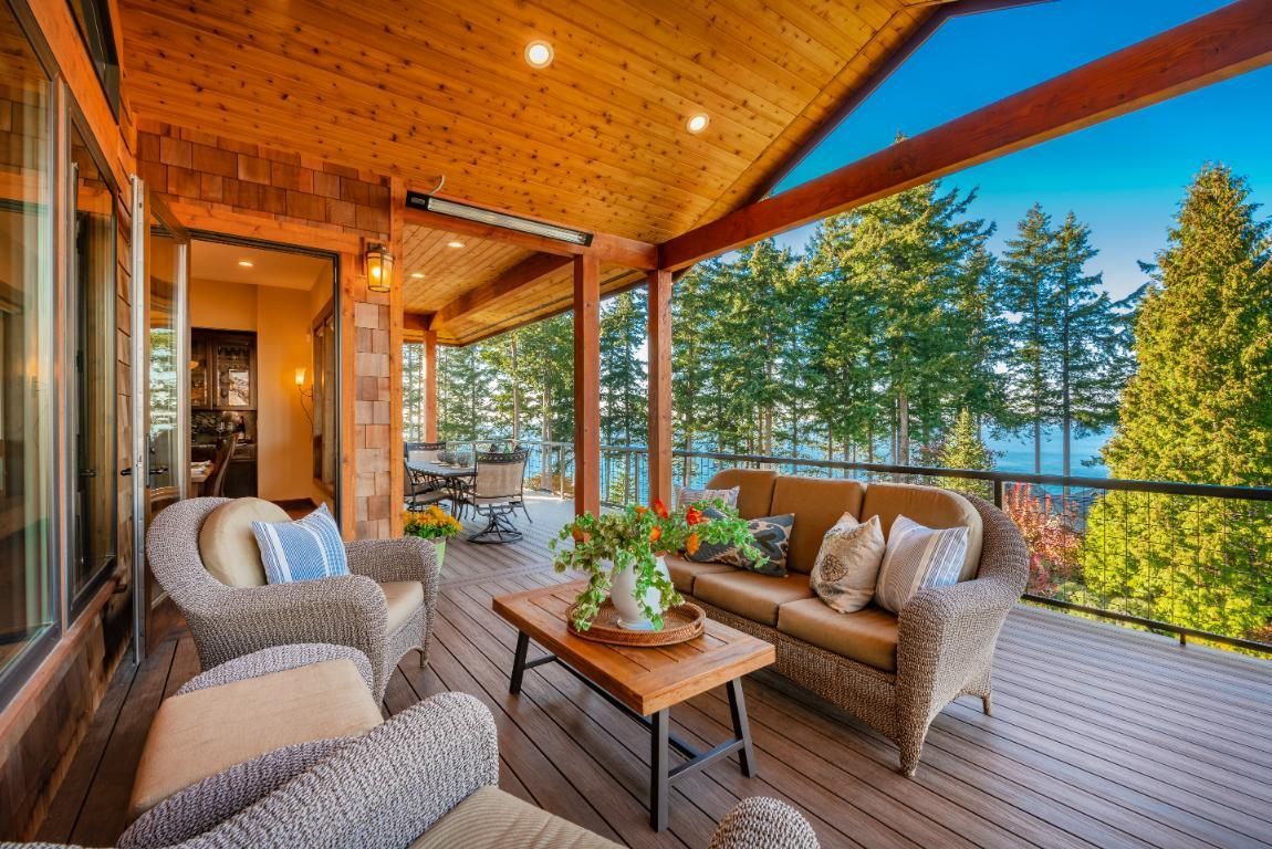A large deck with a couch, chairs and a table overlooking a lake.