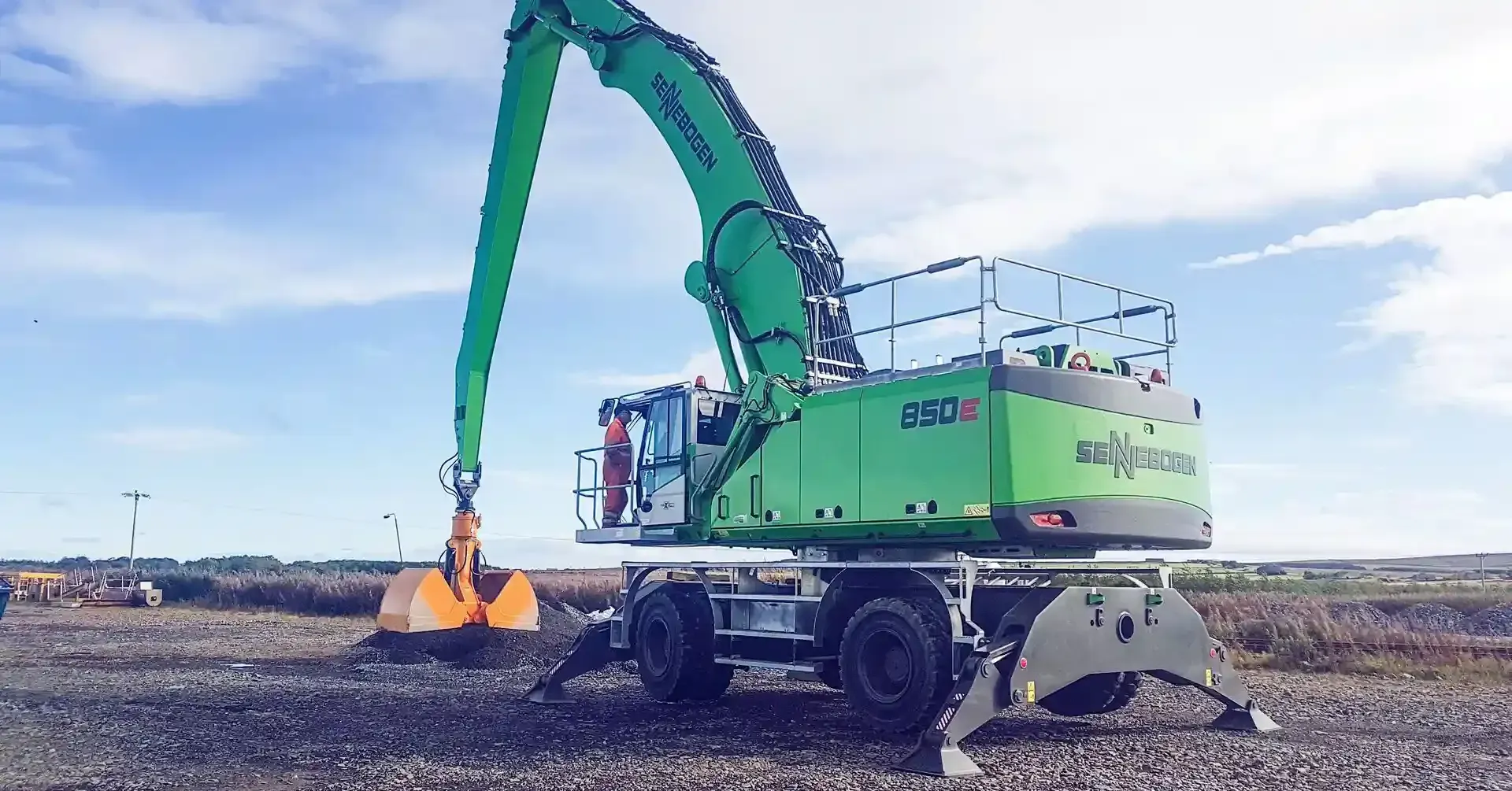 A green excavator is sitting on top of a gravel field.
