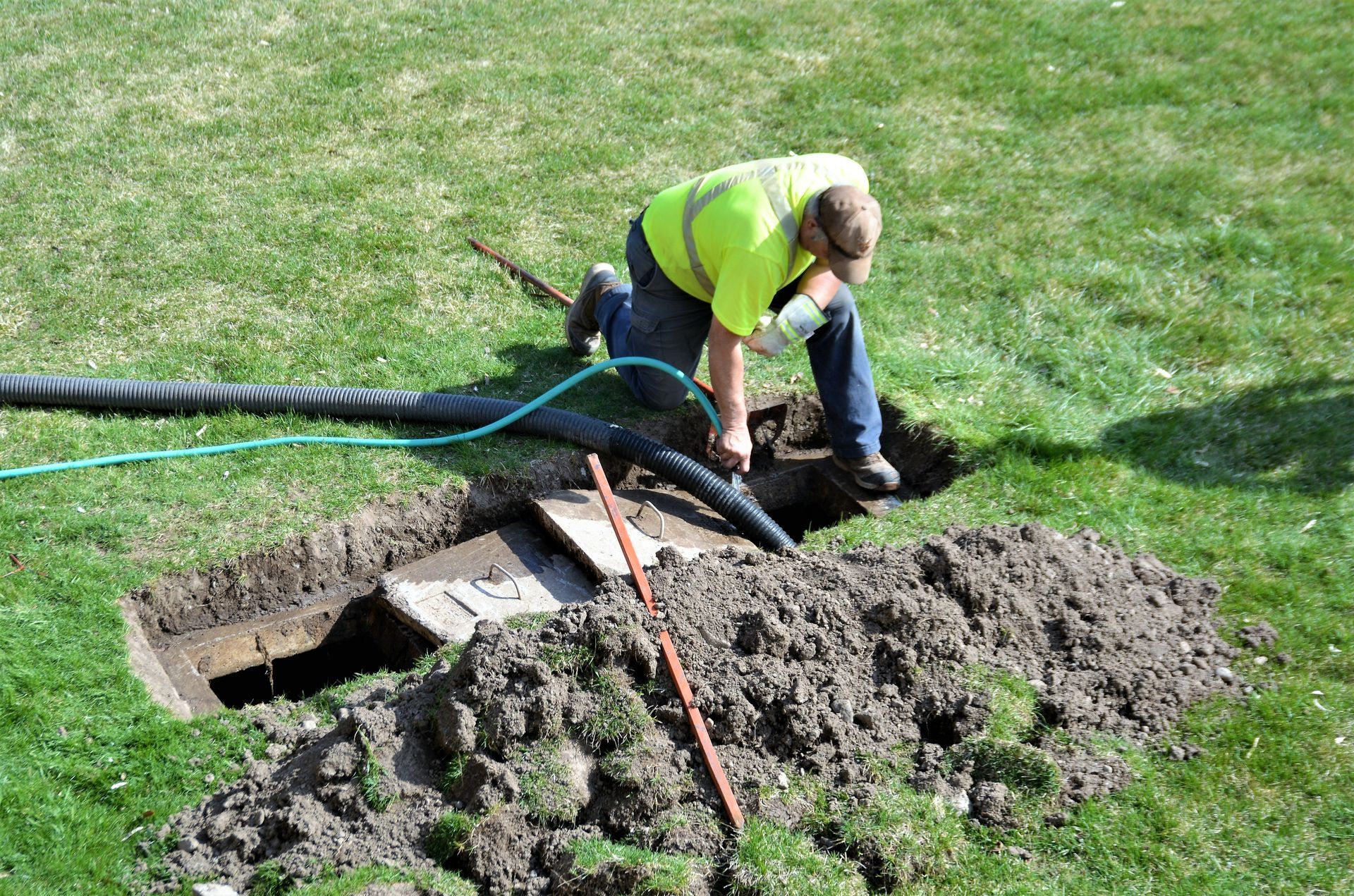 Worker cleaning and servicing a septic tank in a grassy outdoor area.
