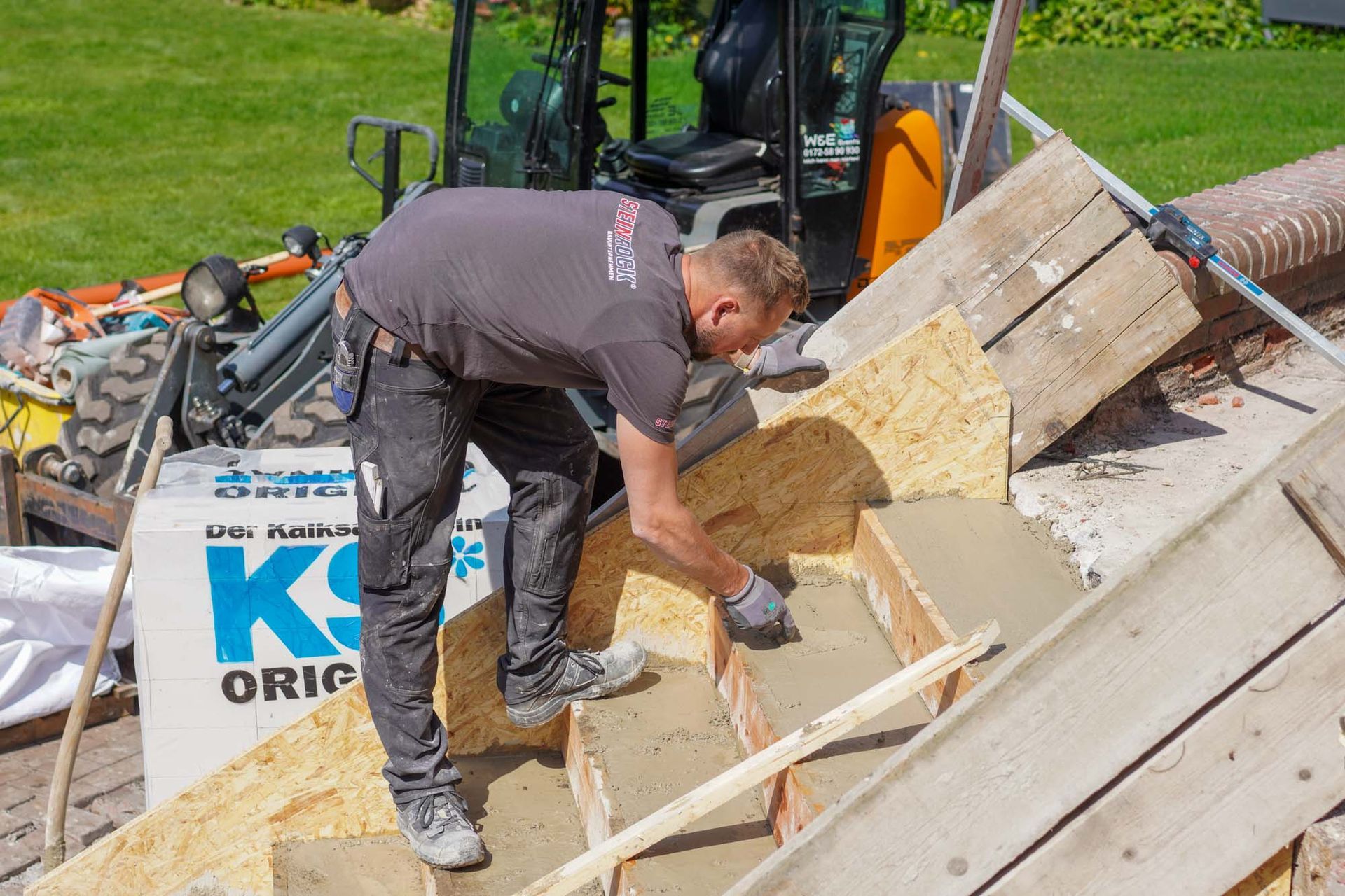 Ein Arbeiter schaufelt Trümmer von einem beschädigten Dach neben einer gelben Baumaschine.