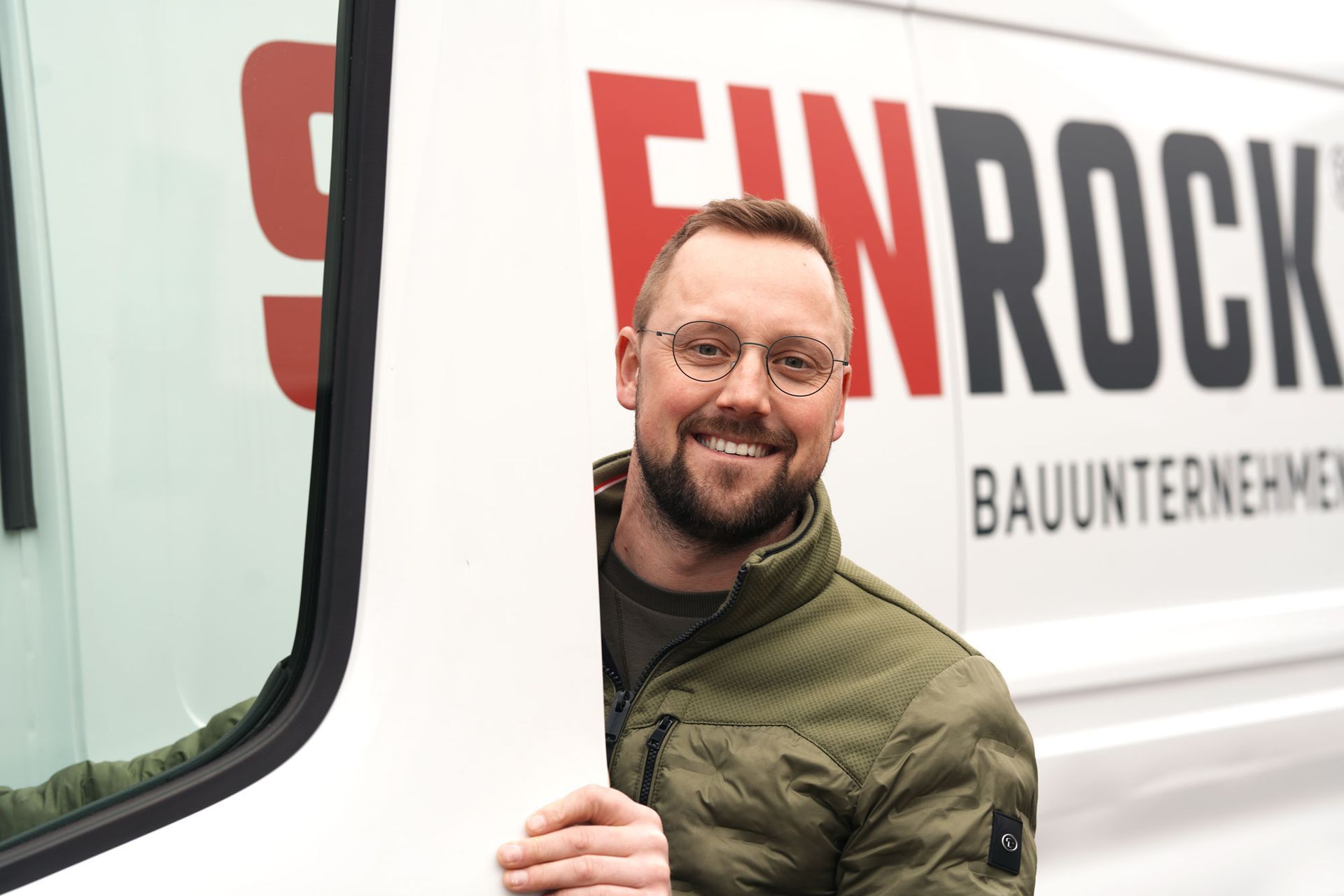 Daniel Neeland lehnt sich aus einem weißen Lieferwagen mit rot-schwarzem Firmenlogo.
