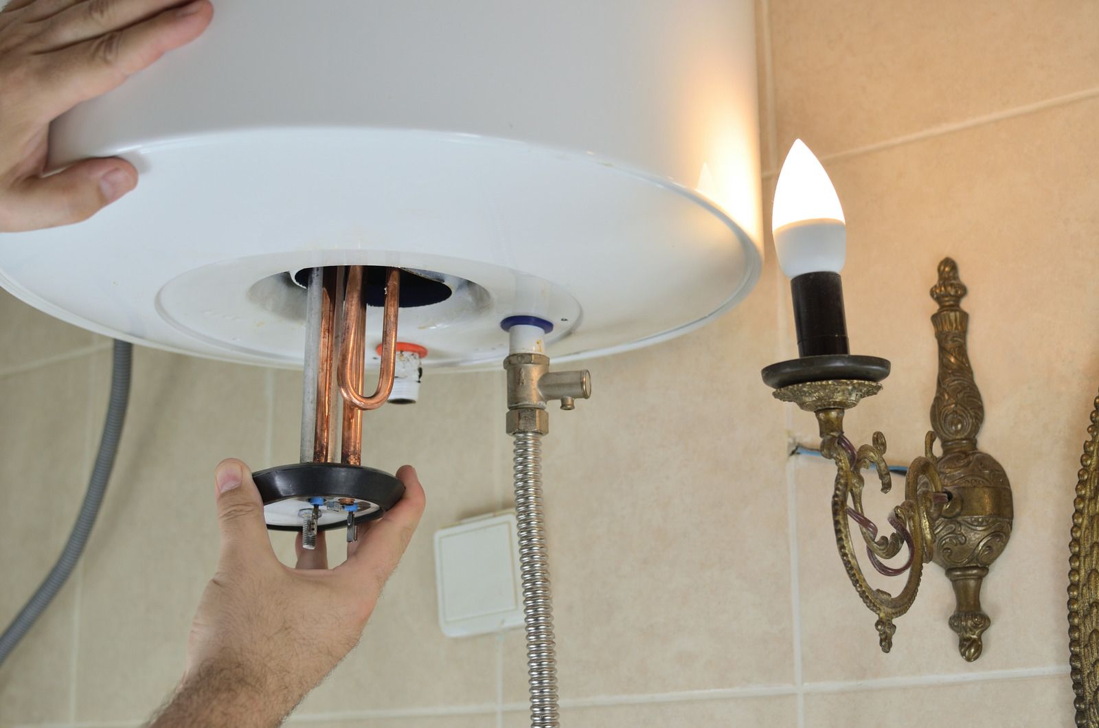 Person installing or repairing a water heater, indoors. White appliance, copper pipes visible.