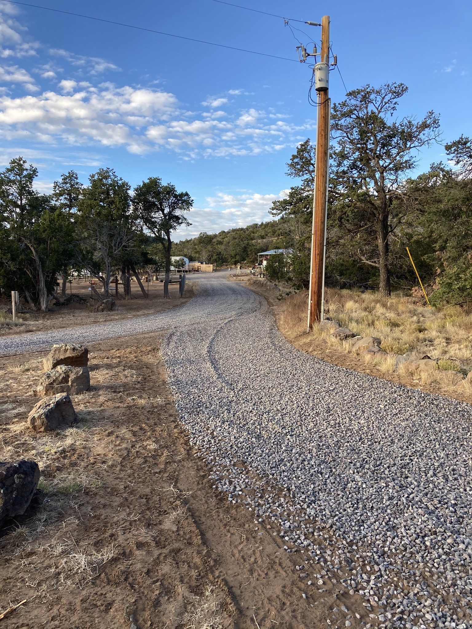 Gravel road through a campground with a utility pole on the right and trees on either side, under a blue sky.