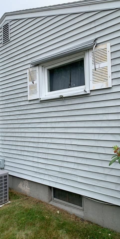 Side of a gray house with white shutters around a window and a basement vent below.