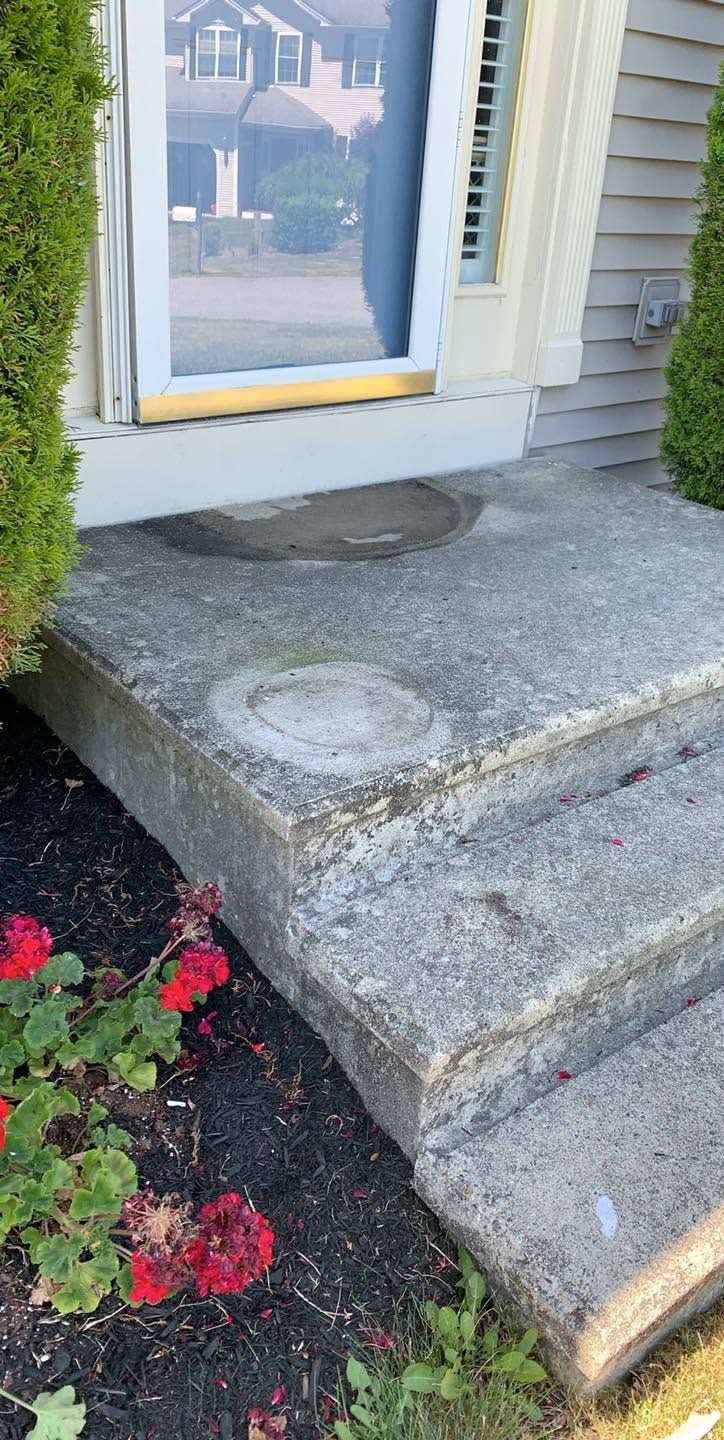 Concrete steps leading to a white front door with a yellow threshold and red flowers nearby