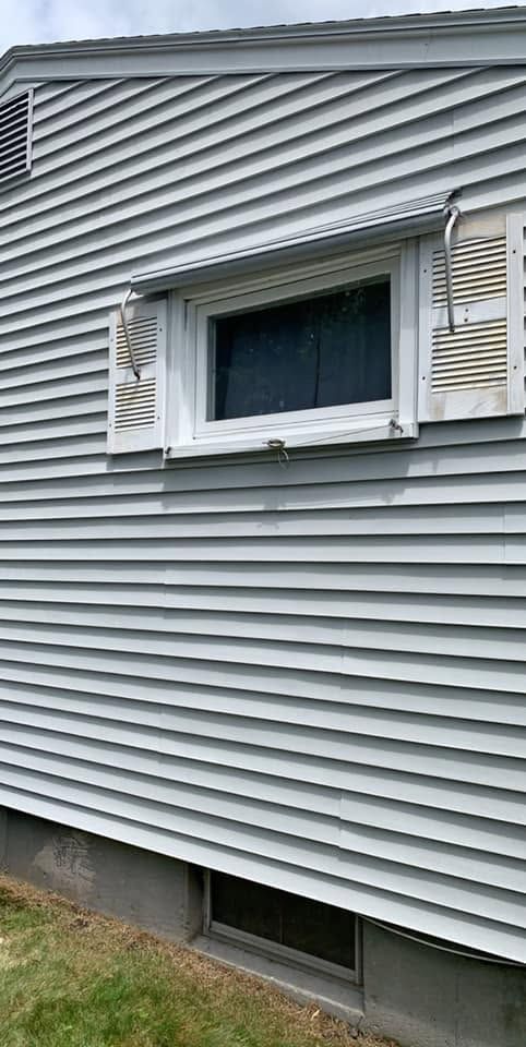 Side of a gray house with a white-trimmed window and shutters, plus a small basement window below.