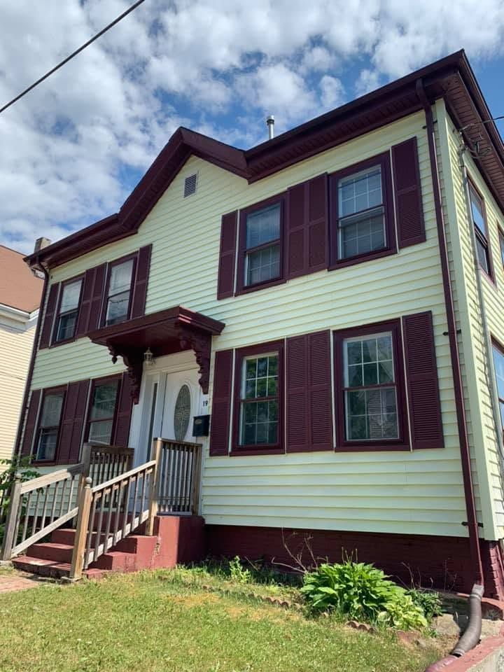 Two-story cream house with burgundy trim, front steps, and small porch under a cloudy sky