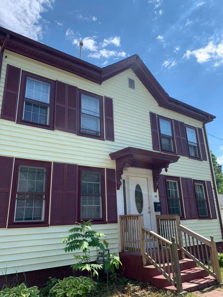 Two-story cream house with maroon shutters and front steps under a blue sky