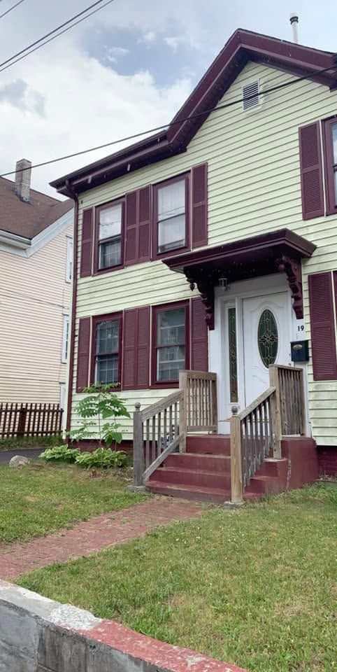 Two-story cream house with burgundy trim, front porch, steps, and small front yard