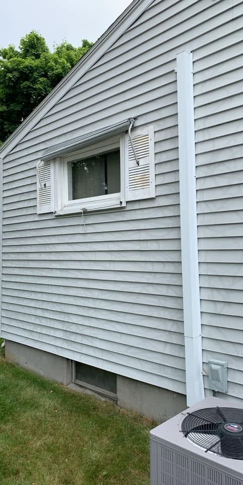 Side of a light gray house with a small white-trimmed window and grass along the foundation.