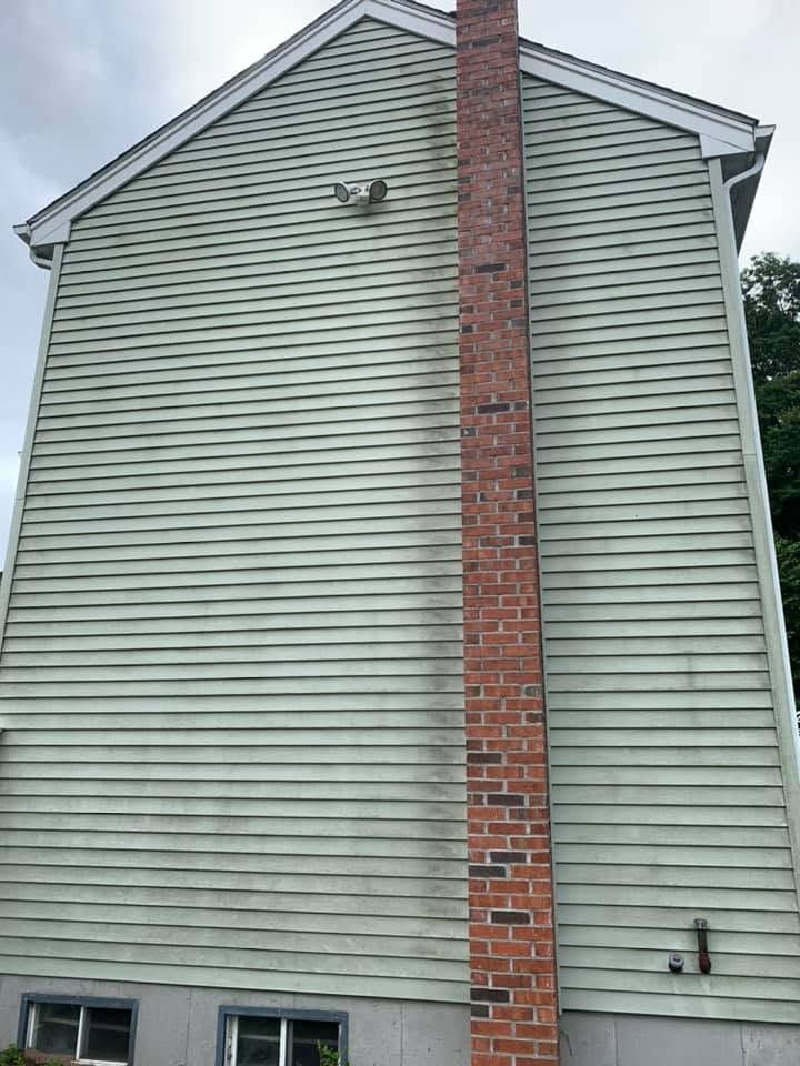 Side of a gray house with a tall red brick chimney and small basement windows