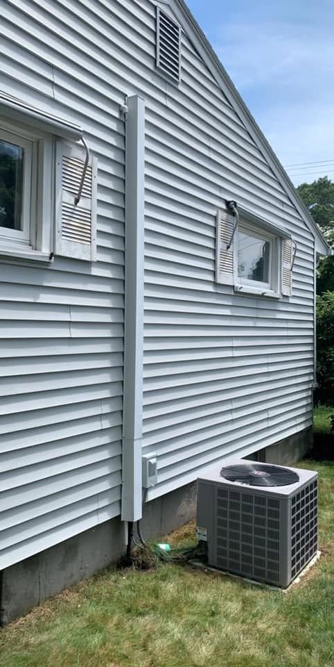 Side of gray house with two windows and an outdoor air conditioner unit on the lawn