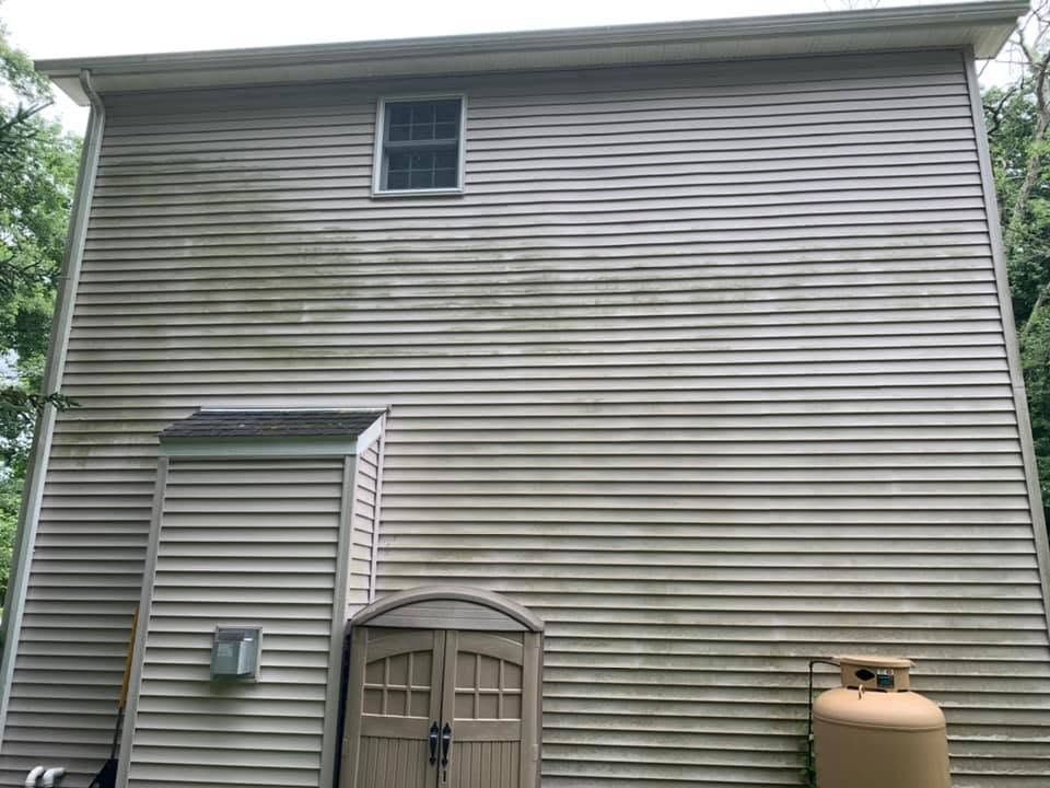 Back of a gray house with horizontal siding, a small upper window, door, and utility meter.