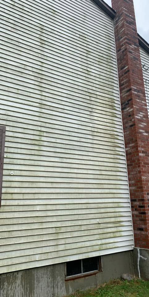 White vinyl-sided house wall with a red brick corner and a small basement window.