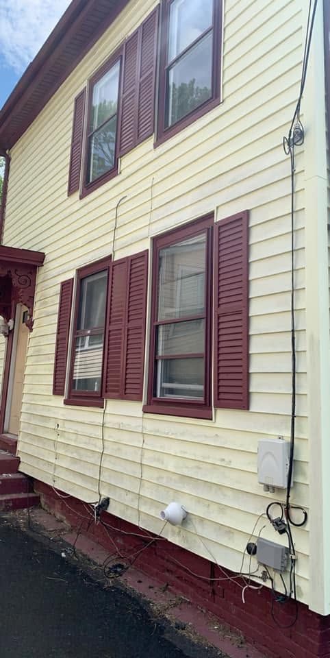Yellow house exterior with maroon shutters, windows, and utility meter by a sloped driveway