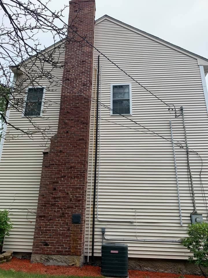 Side view of beige house with brick chimney, two windows, and utility lines outdoors