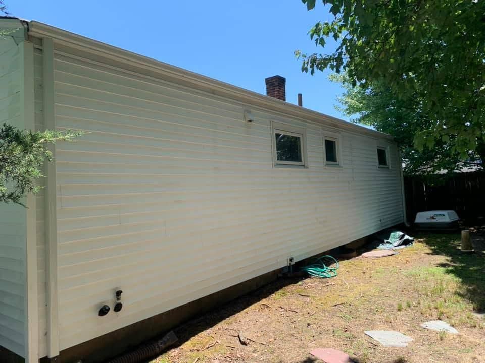 Side view of a beige mobile home with small windows, set on a grassy lot under a blue sky.