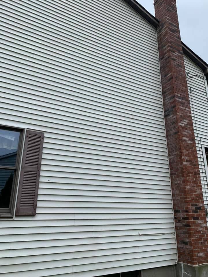 White vinyl house siding beside a red brick chimney and a dark window shutter