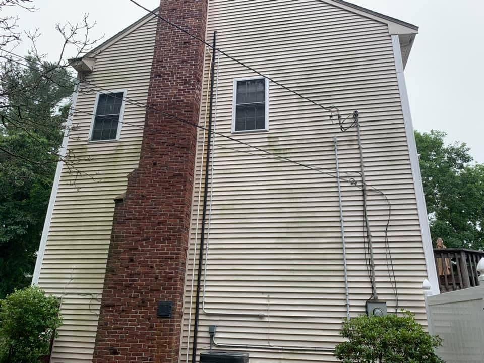 Back of a beige house with a tall red brick chimney and two windows