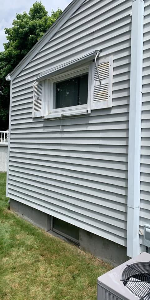Gray-sided house exterior with a small window and white shutters above a grassy yard