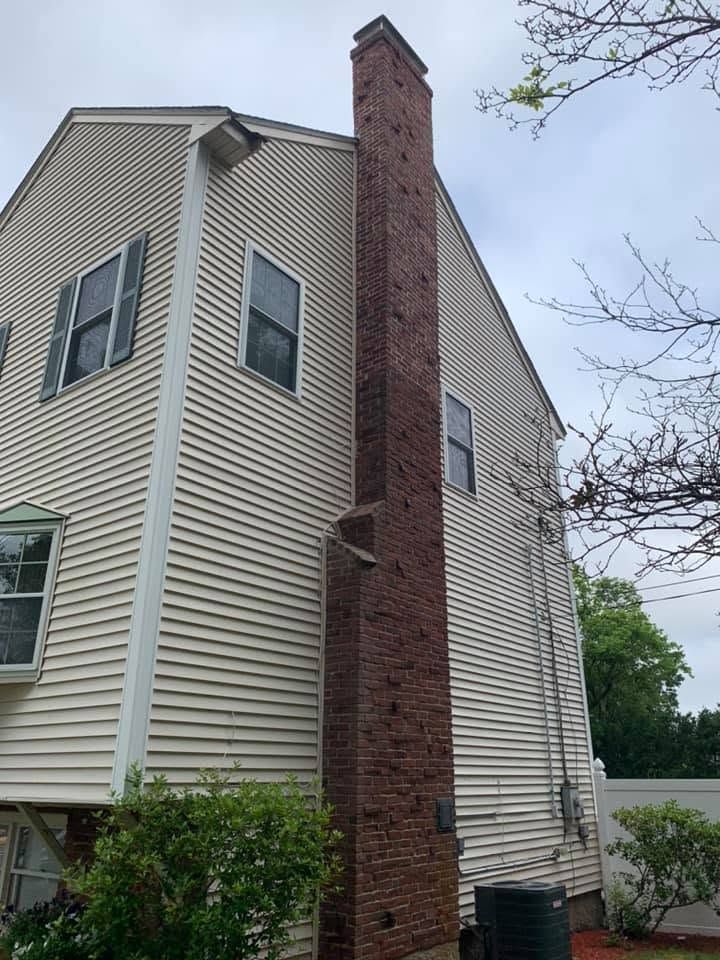 Brick chimney on the side of a beige house with gray trim under an overcast sky