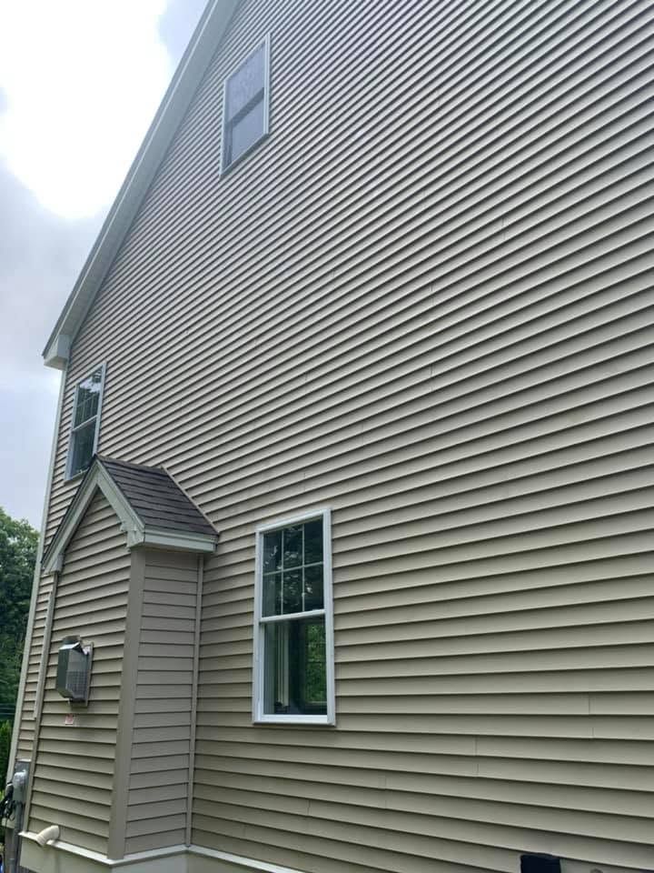 Side view of a beige house with vinyl siding, windows, and a small utility box near the wall.