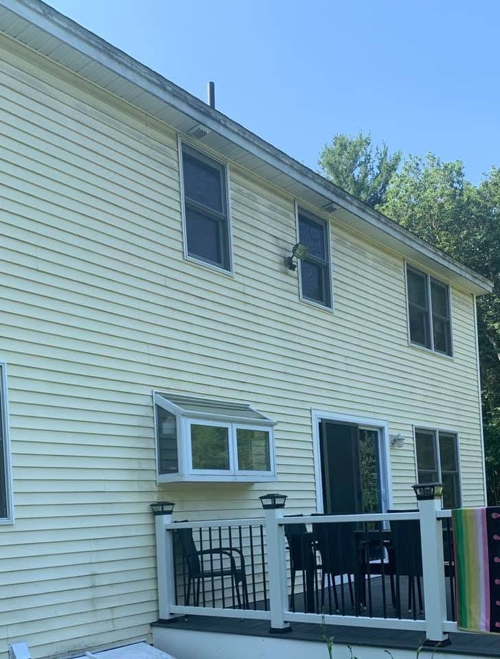 Back of a beige two-story house with white deck railing and a blue sky.