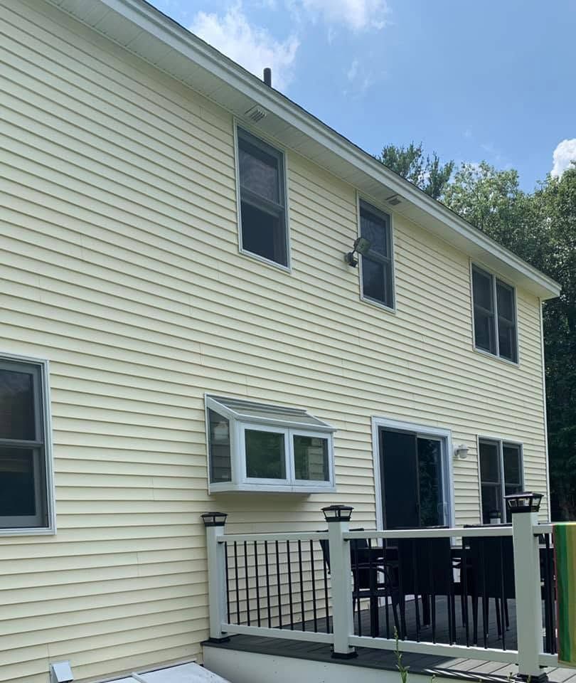 Yellow two-story house exterior with black railing and sliding door on a sunny day