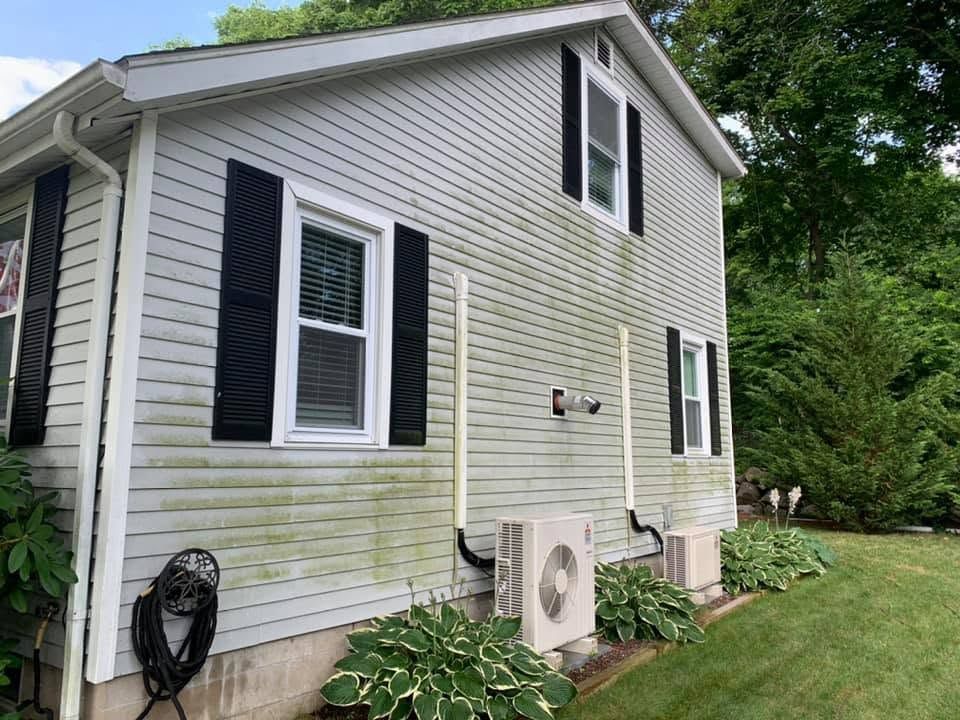 Side of a white house with green staining, black shutters, and an air conditioner unit on a concrete pad
