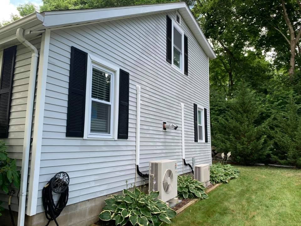 Side of a gray house with white trim, black shutters, an air conditioner unit, and a green lawn.