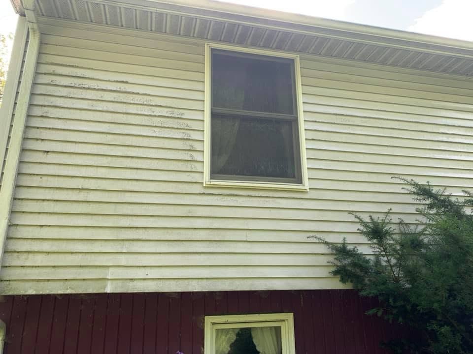 Exterior of a house with beige siding, a dark upper window, and maroon lower wall trim
