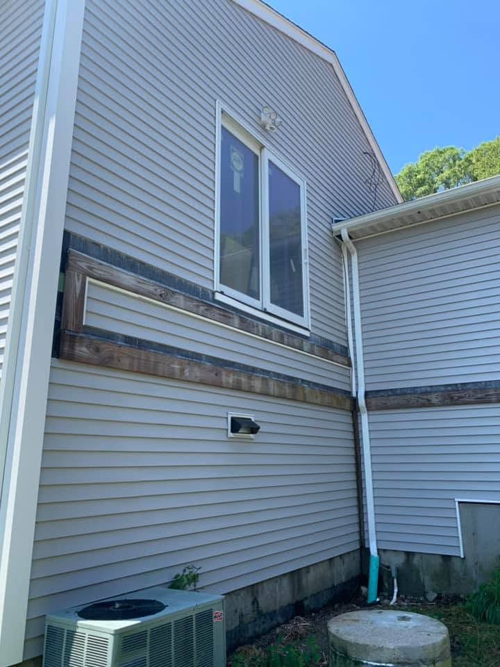 Exterior side of a house with gray siding, windows, an AC unit, and a small concrete pad.