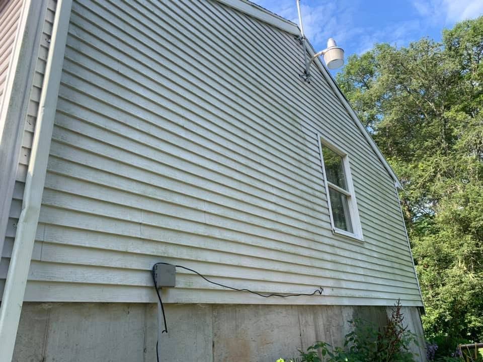 Side view of a white house with vinyl siding, a basement foundation, and trees beside it under a blue sky