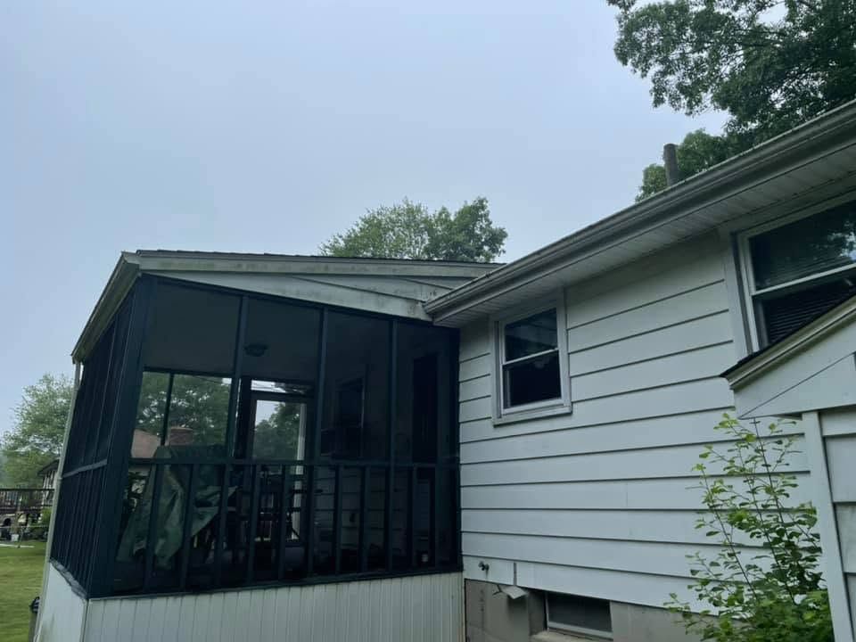 Screened porch with black railing attached to a white house under a cloudy sky