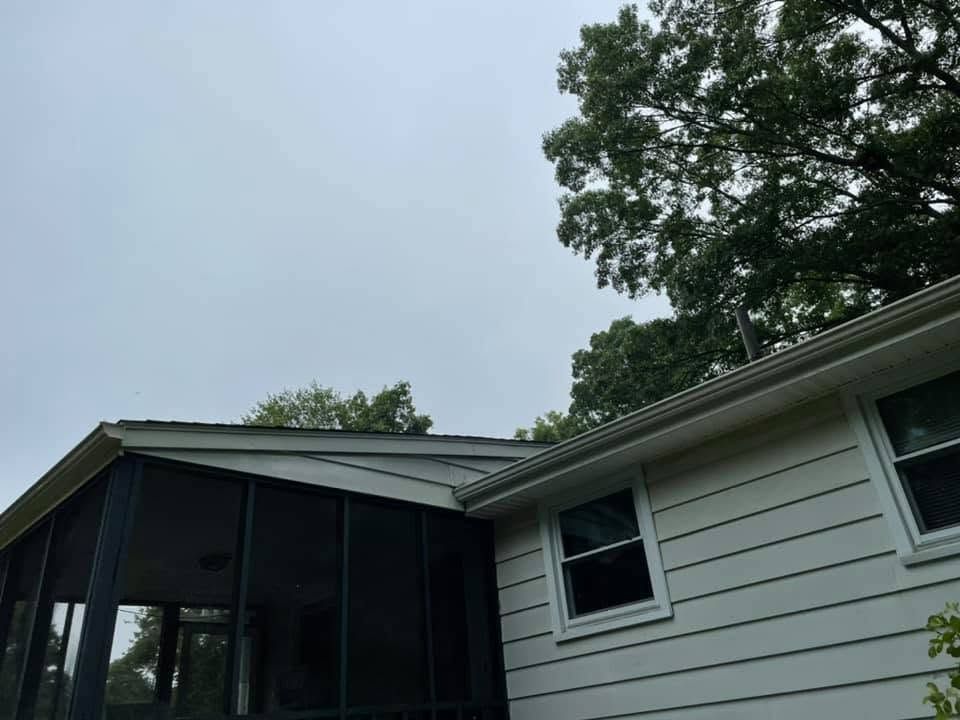 House exterior with screened porch, white siding, and trees under a cloudy sky
