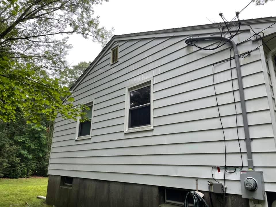 Side of a white house with gray siding, utility meters, and trees beside it.