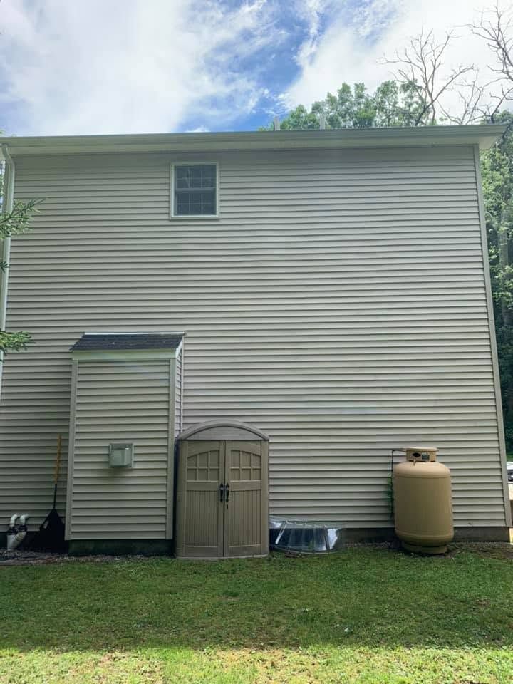 Back of a beige house with a small shed, side door, propane tank, and grassy yard under a blue sky