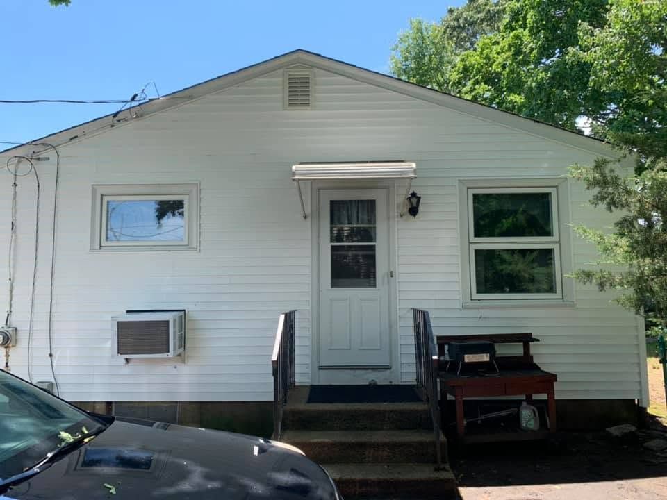 Small white house exterior with front steps, windows, and a window air conditioner.